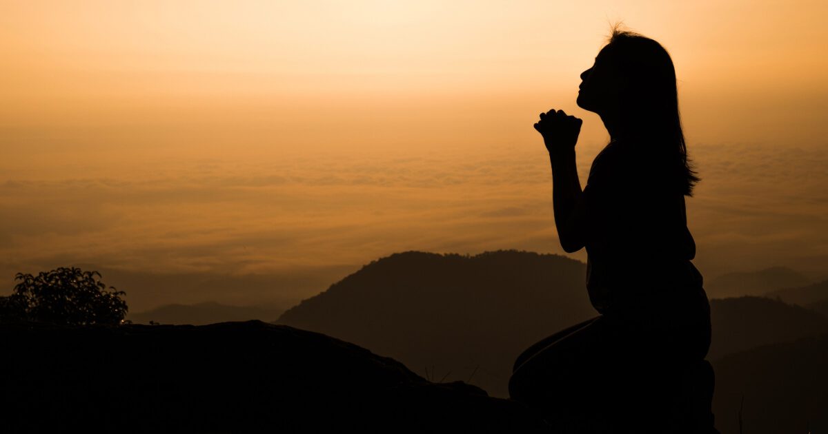 woman kneeling and praying over beautiful sunrise background (Intercession)